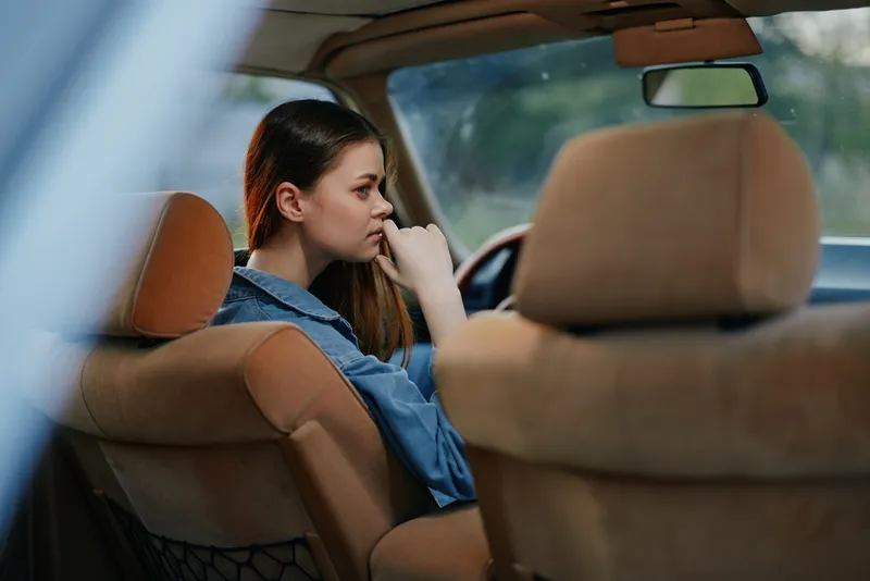 Thoughtful young woman in a car, reflecting on life decisions, dressed casually, with natural light creating a serene mood.