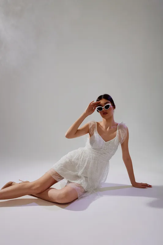 Young woman in a white lace dress and sunglasses poses on the floor in a studio. Concept of woman beauty fashion with elegant and modern style.