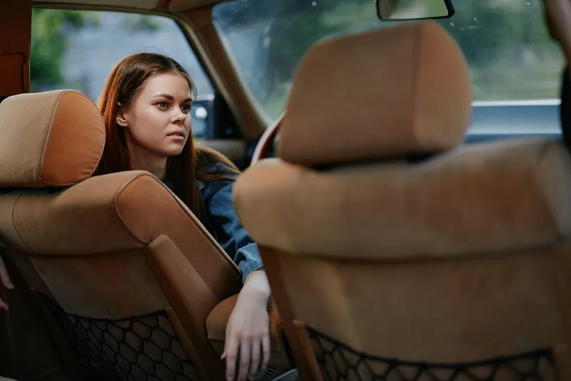 Young woman in casual attire sitting in car relaxing, showcasing thoughtful expression and natural light, ideal for lifestyle themes.