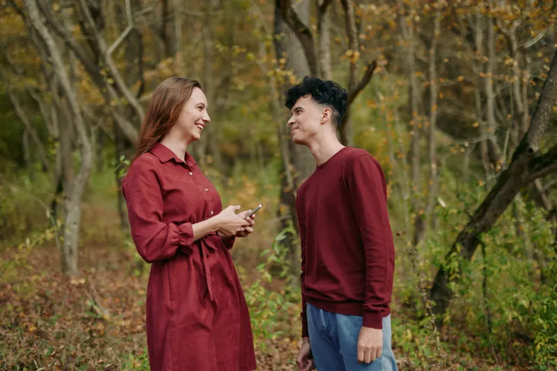 Candid portrait of a young couple sharing a genuine moment in a woodland clearing, an authentic interaction captured on a phone amidst warm autumn colors and natural relaxed expressions.