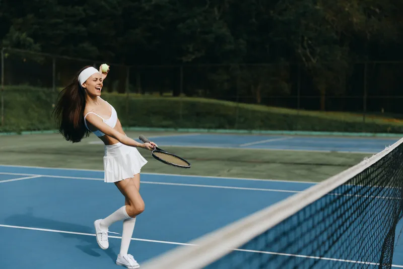 Young female tennis player enjoying a sunny day on the court, wearing a stylish sports outfit, showcasing joy and energy during a match with a green backdrop