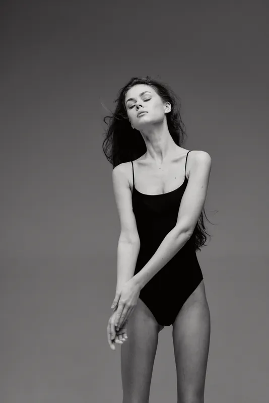 Elegant black and white woman posing in a black swimsuit with closed eyes and relaxed expression