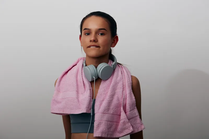 Woman fitness sport athlete after a workout, portrait with headphones and towel, athletic vibe and focused expression against a plain studio backdrop.