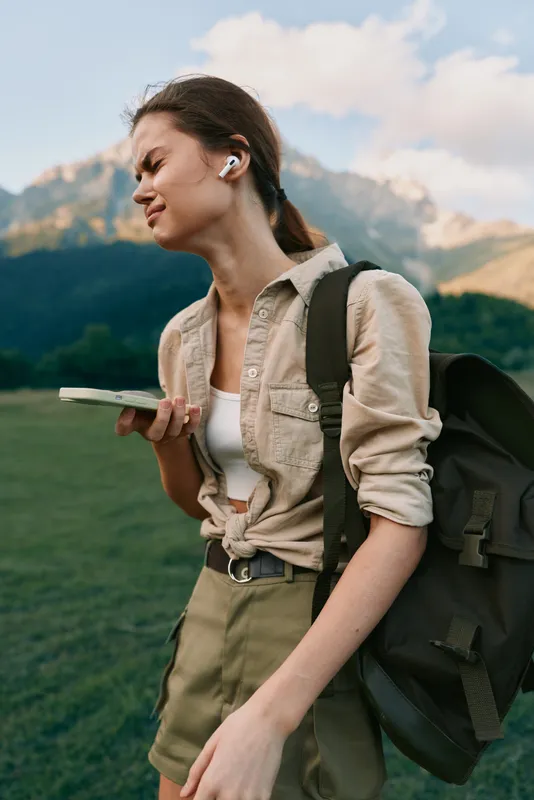 A woman hiker with a backpack and headphones walks outdoors, phone in hand, a lifestyle portrait capturing adventure, exploration, and everyday wellness