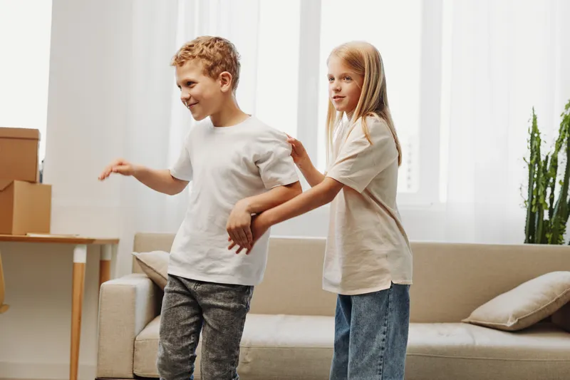 Two happy kids playing together indoors near sofa in bright living room with natural light. Concept of childhood fun and sibling bonding at home.