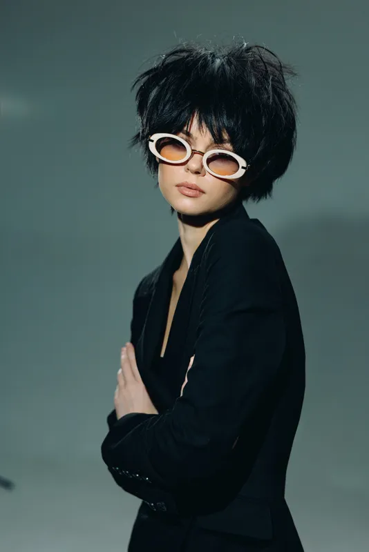 Stylish woman wearing white sunglasses and black outfit posing confidently with folded arms