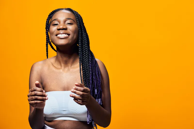 Happy young woman with braided hair smiling, wearing a white top, against a vibrant yellow background, capturing joy and positivity in a colorful setting