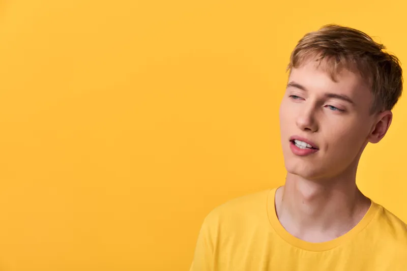Young man in a yellow tee against a bright background, relaxed pose and subtle smile, casual fashion vibe, clean studio shot with minimal styling and warm lighting for lifestyle branding and