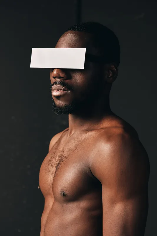 Creative conceptual portrait of African man with dark skin and muscular body in studio lighting. Artistic visual style with paper strip covering eyes for anonymity and mystery.
