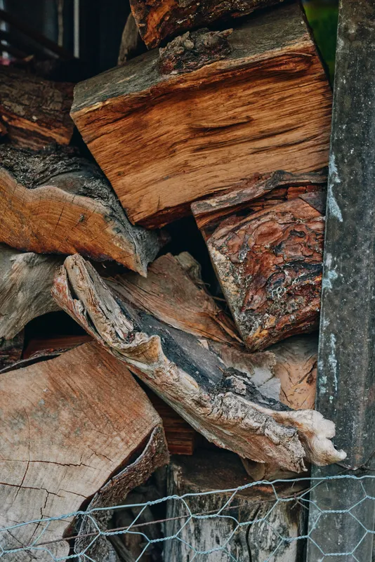 Firewood, woodpile, logs, split wood, rustic, stacked close-up of seasoned oak and birch split wood in a rural wood shed, textured bark and chicken wire front, fireplace fuel for winter.