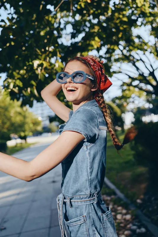 Lifestyle woman in modern boho-western denim street style wearing blue sunglasses and a red bandana outdoors, captured in vibrant film color for a trendy summer vibe.