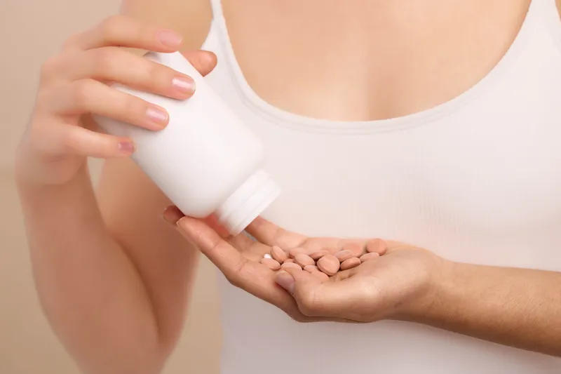 an asian woman pours pills from a bottle onto her palm in a close up shot, showcasing medication care and health awareness with soft lighting and a calm tone.