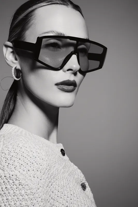 White woman with light skin wears large black sunglasses and knitted sweater on grey background, fashion and style concept.
