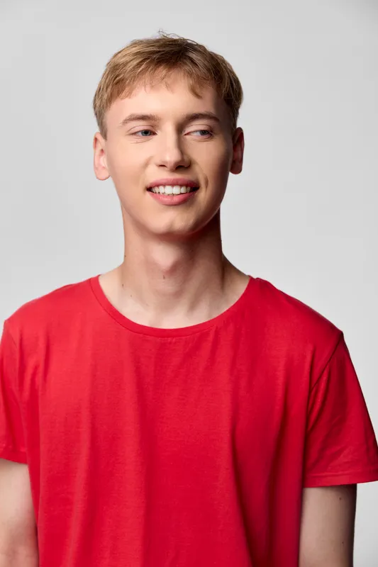 Smiling young man wearing a red casual t shirt in a studio with clean background and natural lighting, showcasing approachable style and everyday fashion appeal