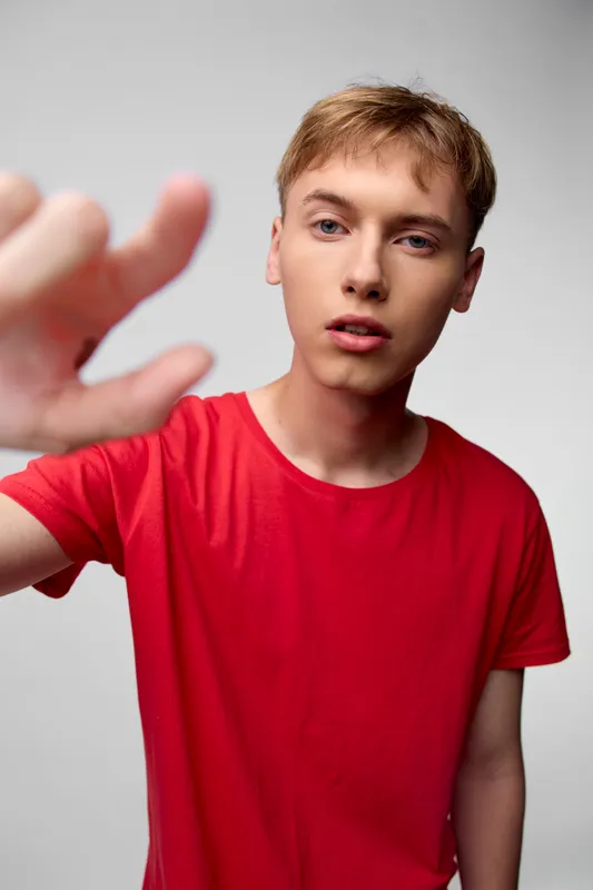 Close up of a young man in a red shirt reaching toward the camera, creating a sense of motion and urgency, studio setting with soft lighting and a clean background, focal point on the outstretched