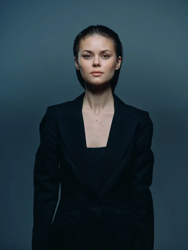 Portrait of a serious young woman in a black blazer with wet hair and intense gaze against a dark background.