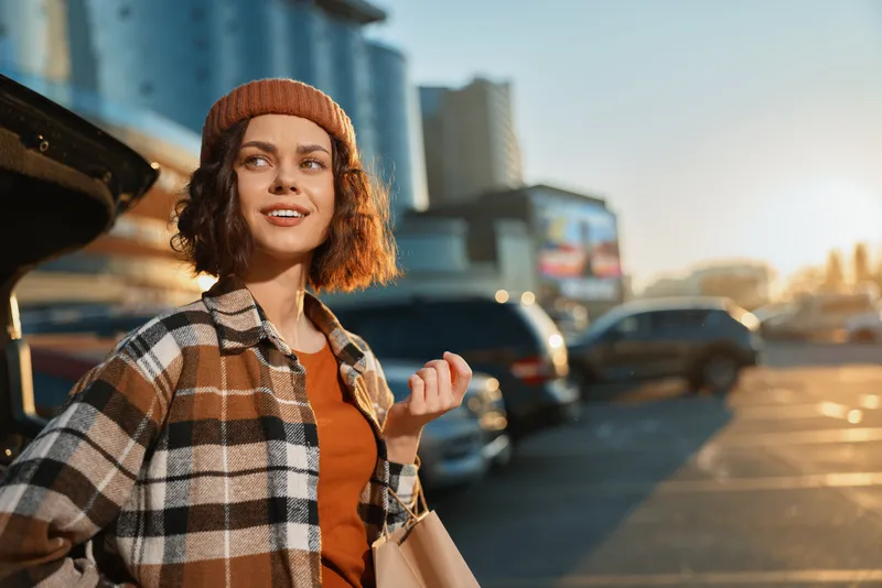 Woman urban shopping portrait candid golden lifestyle scene with beanie and paper bag in a sunlit parking lot, authenticity and golden hour glow capture mindful living and emotional storytelling.