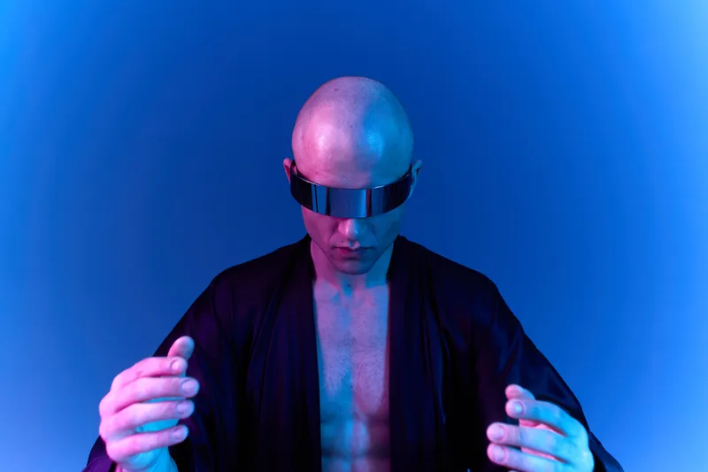 Futuristic man with a bald head, wearing sleek sunglasses, is immersed in a captivating blue light, exuding a unique blend of mystery and innovation.
