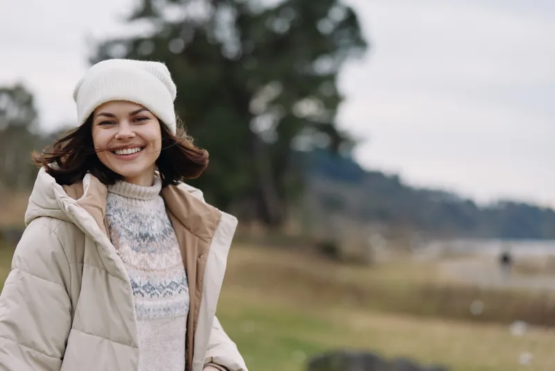 Winter outdoor smiling portrait of a woman wearing a jacket and beanie, enjoying a crisp day in a wide landscape with open space, soft daylight and calm nature.
