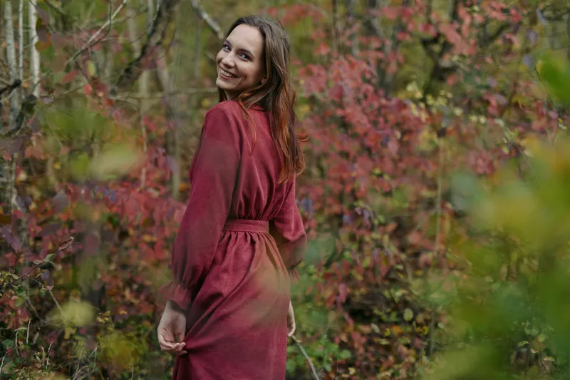 A candid portrait of a smiling woman in a red dress among autumn foliage, capturing natural movement and light, conveying authenticity and credibility in lifestyle and portrait storytelling.