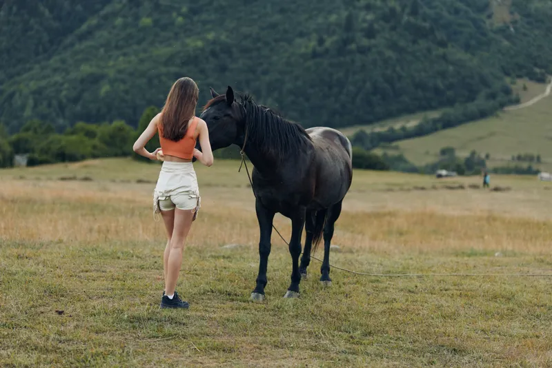 A young woman stands in an open field facing a calm horse, sharing a quiet moment in nature and feeling a gentle connection that conveys freedom, peace, and simple rural charm.