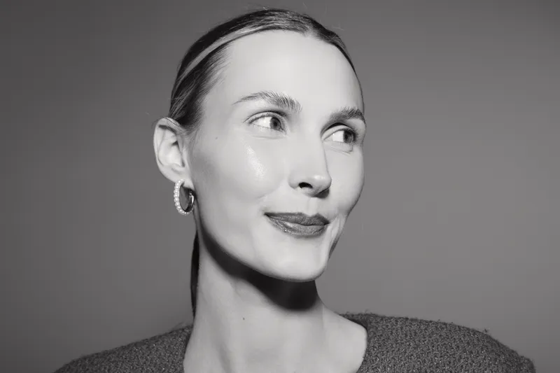 Portrait of a smiling Caucasian woman with pale skin and slicked back hair looking sideways. Studio lighting highlights her facial features against a plain background. Concept for beauty and