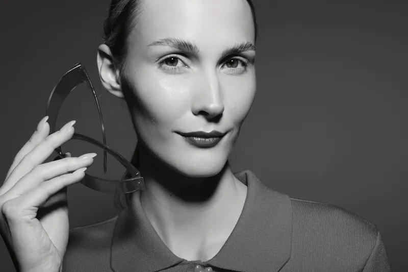 Portrait of a young white woman with fair skin holding eyeglasses near her face, looking confident and composed. Concept for vision, eyewear, and fashion.