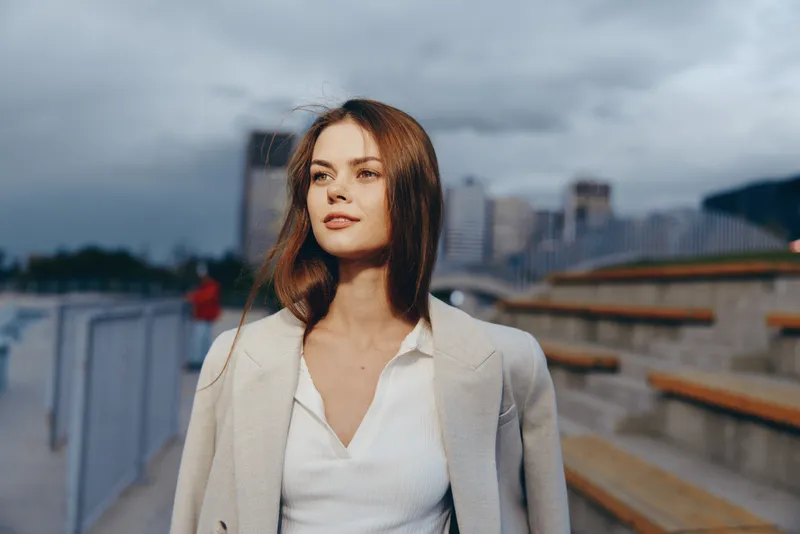 Confident woman in business attire smiling against urban backdrop, embodying empowerment and professionalism in a modern setting.