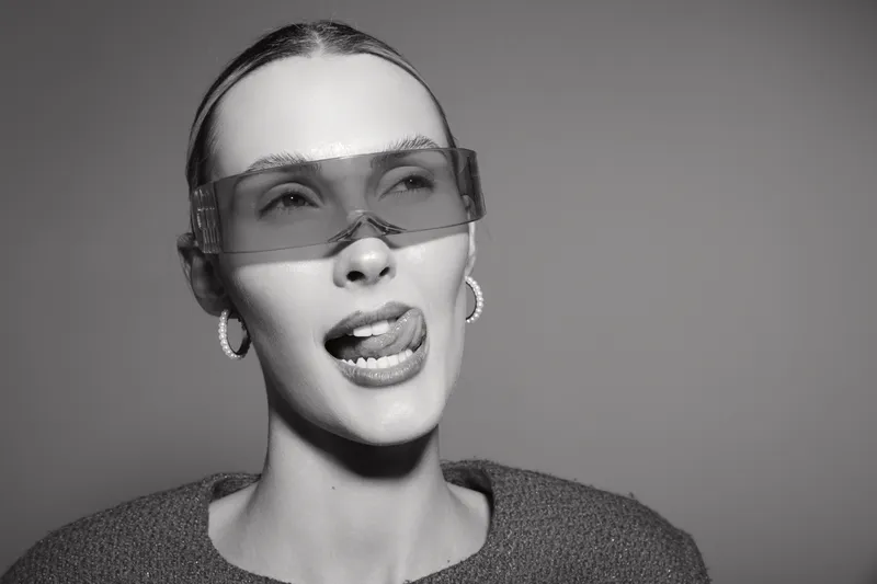 Young white woman with fair skin and clear glasses makes playful face in studio. Concept for emotions, youth, and modern fashion portrait photography.
