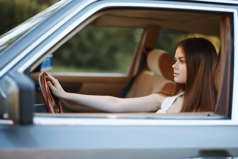 Young woman with long hair sitting in a vintage car, showing confidence and style, immersed in thoughtful reflection, summer vibes.