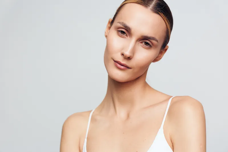 Woman applying face cream, close up portrait against clean white background. Smooth skin and calm expression convey skincare, beauty, wellness, and selfcare. Soft studio light.