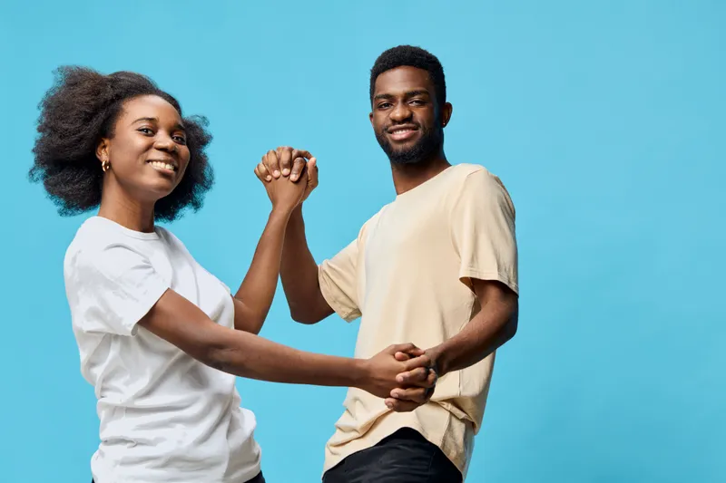 A joyful young couple dancing together against a bright blue background, showcasing love, happiness, and connection in casual attire
