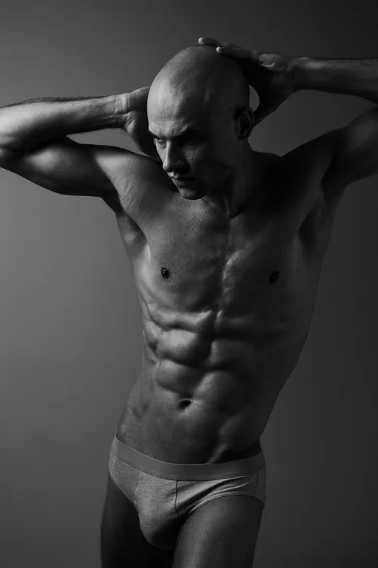 Black and white portrait of a man showcasing a strong physique, exuding confidence and strength in a dynamic pose with dramatic lighting.