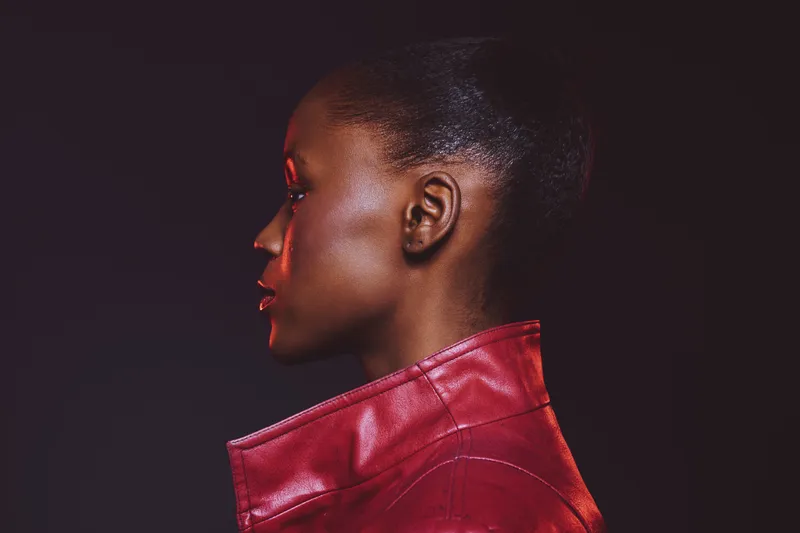 Profile of a dark skinned African woman with natural hair wearing a red leather jacket. Studio portrait on black background with dramatic lighting, concept for fashion and beauty.