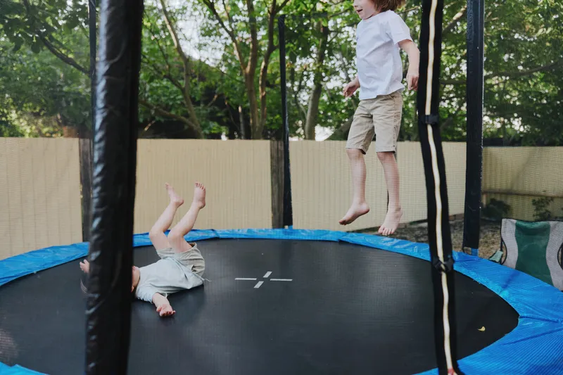 Happy kids jumping on a trampoline, enjoying playful moments in the sunny backyard, filled with laughter and excitement, showcasing childhood joy.