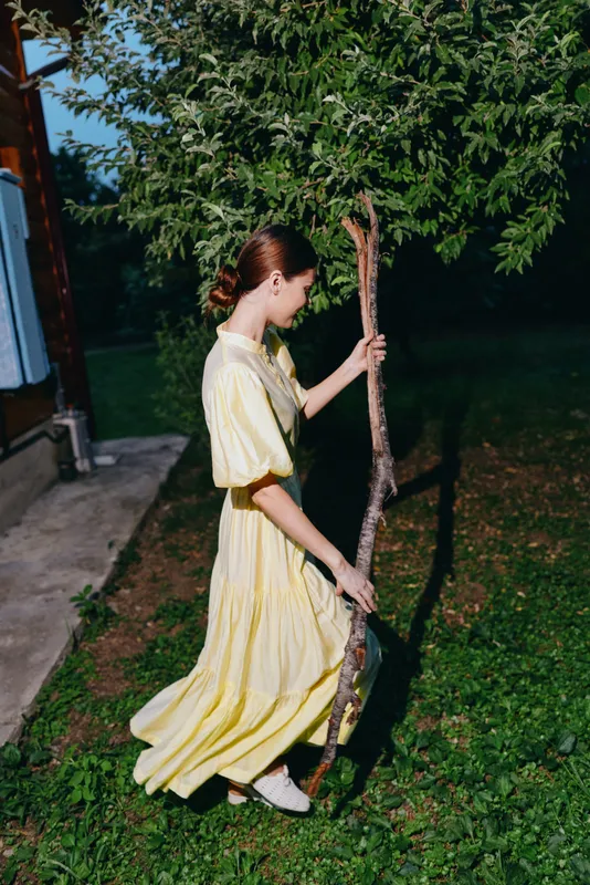 Woman in yellow dress holding tree branch outdoors at dusk, authenticity inclusivity in portrait