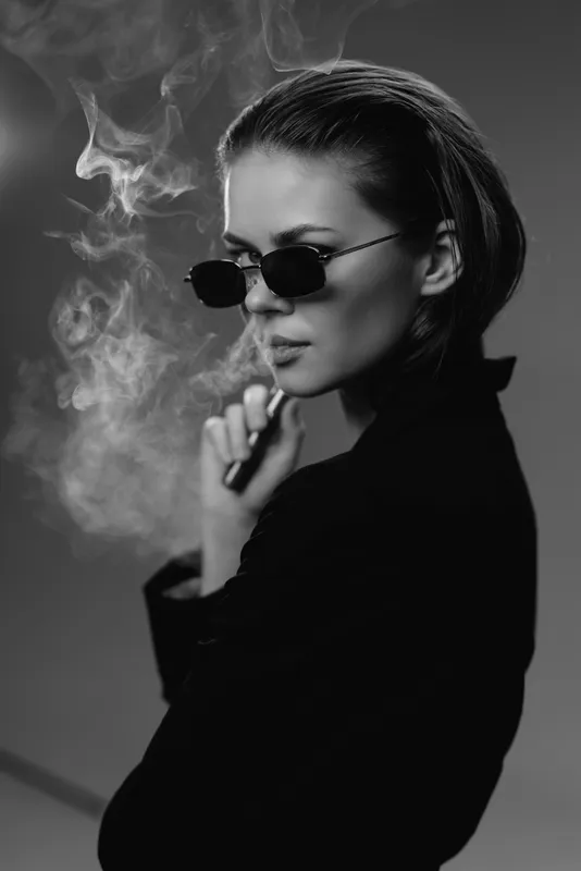 Stylish woman wearing sunglasses smoking in black and white with mysterious expression and smoke around