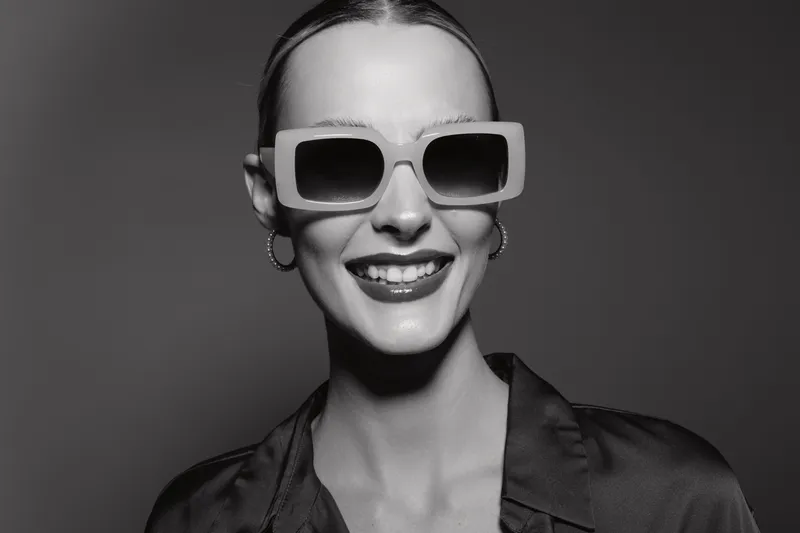 Happy Caucasian woman with pale skin wears large sunglasses and smiles confidently in studio lighting.
