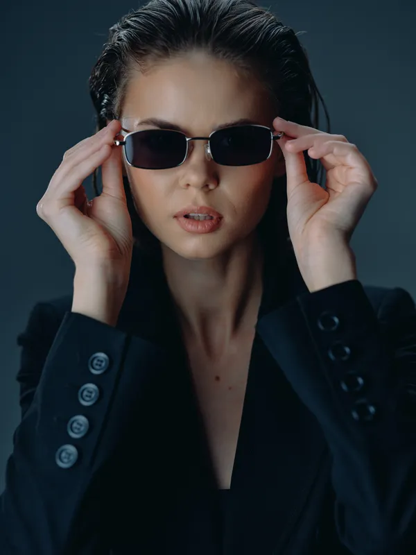 Stylish woman adjusting sunglasses wearing dark blazer with wet hair and serious expression