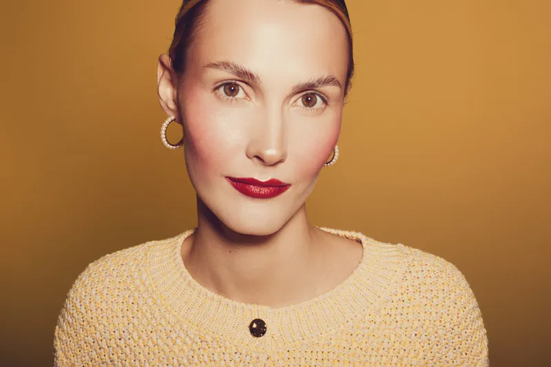 Close-up portrait of a confident woman with red lipstick and hoop earrings wearing a knitted sweater against a warm brown background. Concept of beauty and fashion.