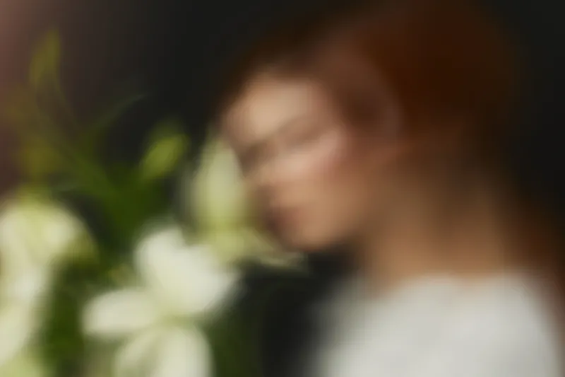 Blurred portrait of a model with red hair surrounded by white flowers, capturing emotions of calmness and elegance in a soft, dreamy atmosphere