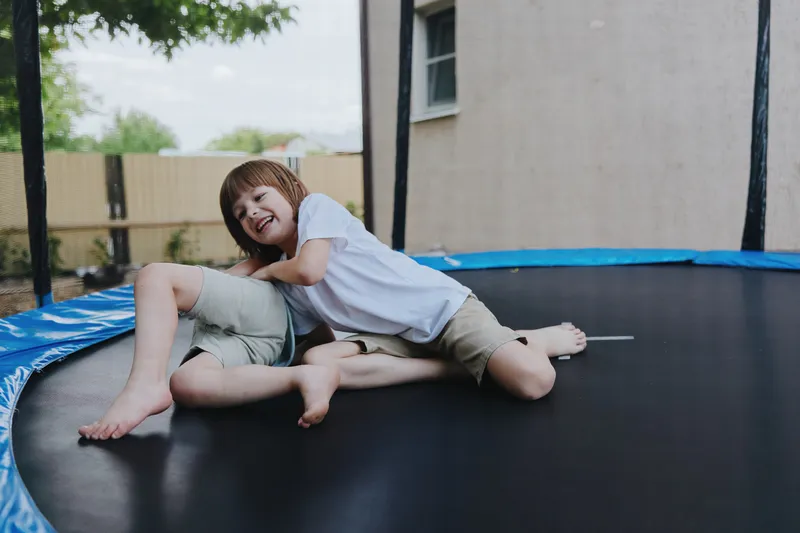 Playful boy enjoying a sunny day, jumping on a trampoline, wearing casual clothes, with a joyful expression and vibrant outdoor background.
