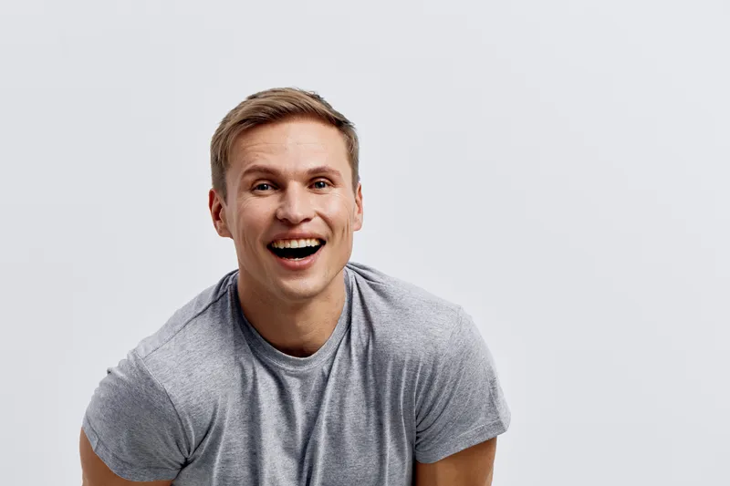 smiling man in gray t-shirt laughing cheerful happy casual wear studio portrait isolated on light background mental health and gadgets concept
