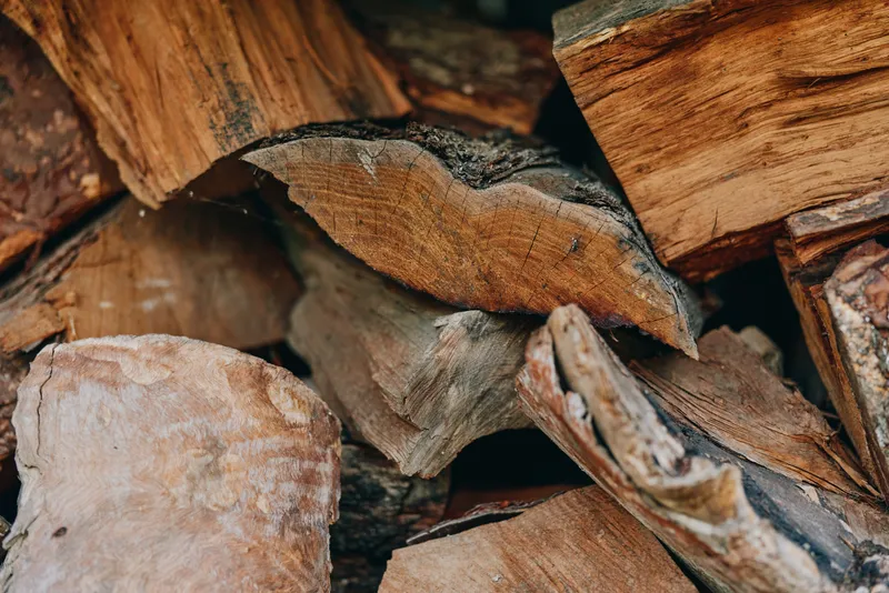 Closeup of stacked wood and chopped logs in a rustic woodpile showing bark and split firewood textures, seasoned hardwood for fireplace fuel and winter preparation.