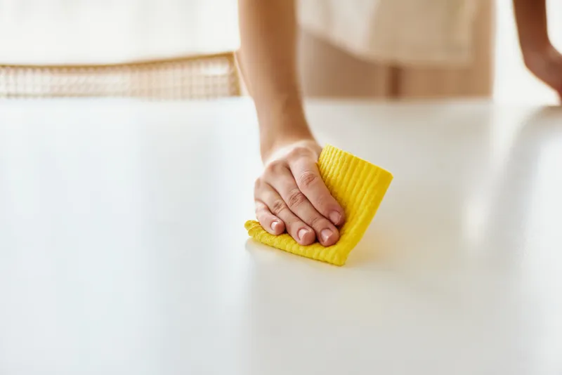 Cleaning, hand, cloth, table, wipe Closeup of a person wiping a white table with a yellow cloth, domestic surface cleaning for hygiene, household maintenance and gentle wiping motion.