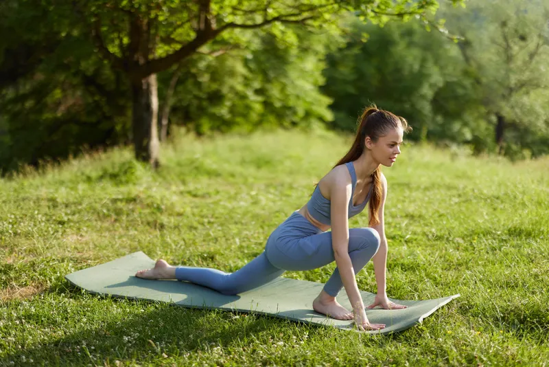 Young woman practicing yoga in a serene outdoor setting, showcasing flexibility and mindfulness in comfortable athletic wear during a sunny day