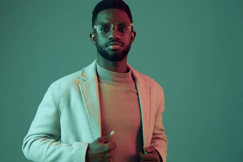Stylish young man in casual attire with glasses, showcasing confidence against a colorful background, perfect for fashion and lifestyle concepts