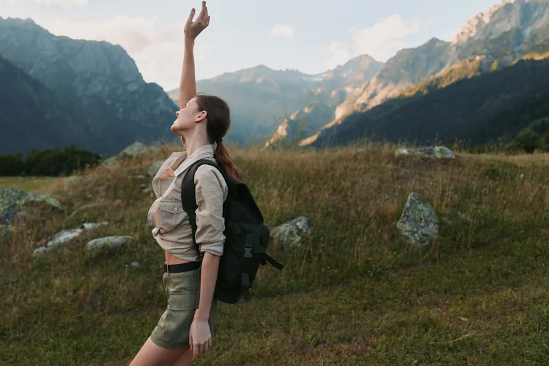 Woman hiking outdoors in a dramatic mountain landscape with a backpack, exuding adventure and freedom amid rugged terrain under a scenic valley and clear sky.