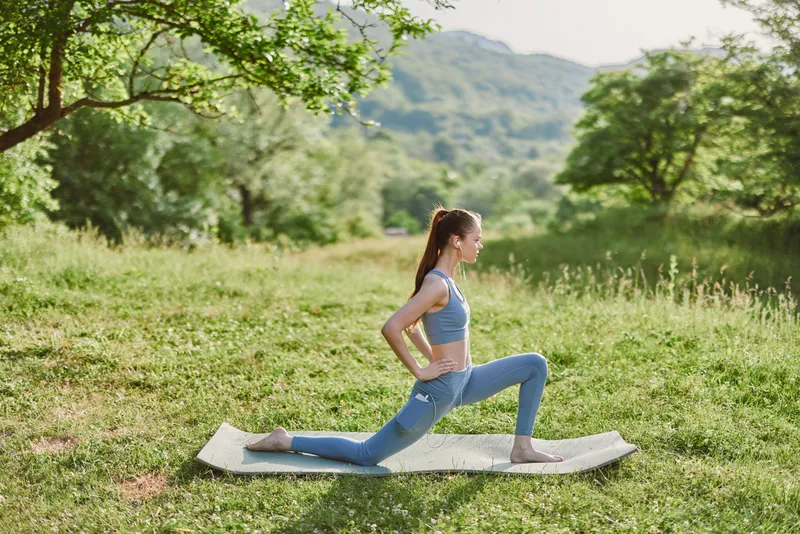 Young woman practicing yoga in a serene outdoor setting, showcasing a healthy lifestyle with vibrant green nature, flexibility, and tranquility
