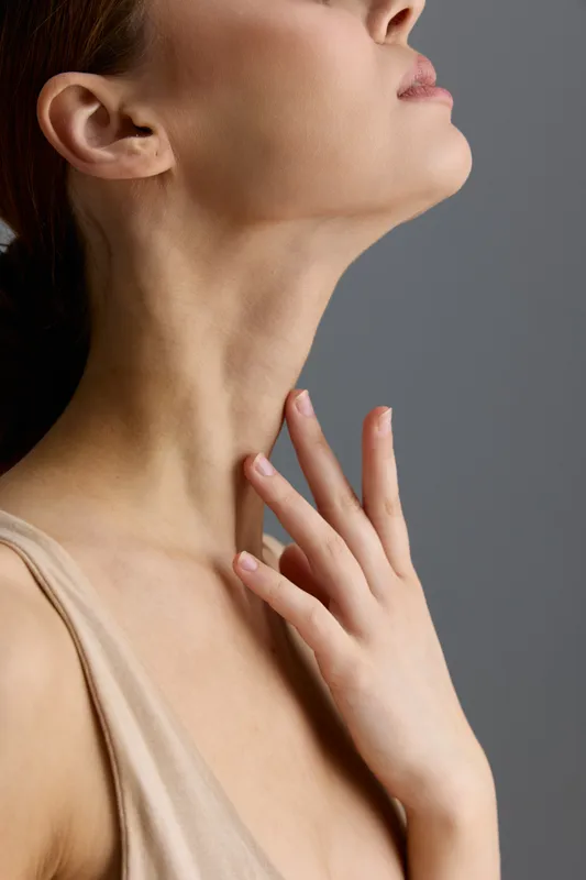 close-up woman neck and hand with smooth skin, natural light, soft beige top, delicate skin texture, minimalistic gray background, skincare concept